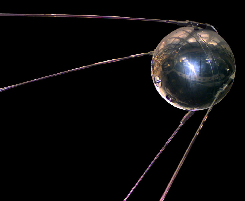 A round metallic satellite with trailing antennae floats on a black background.