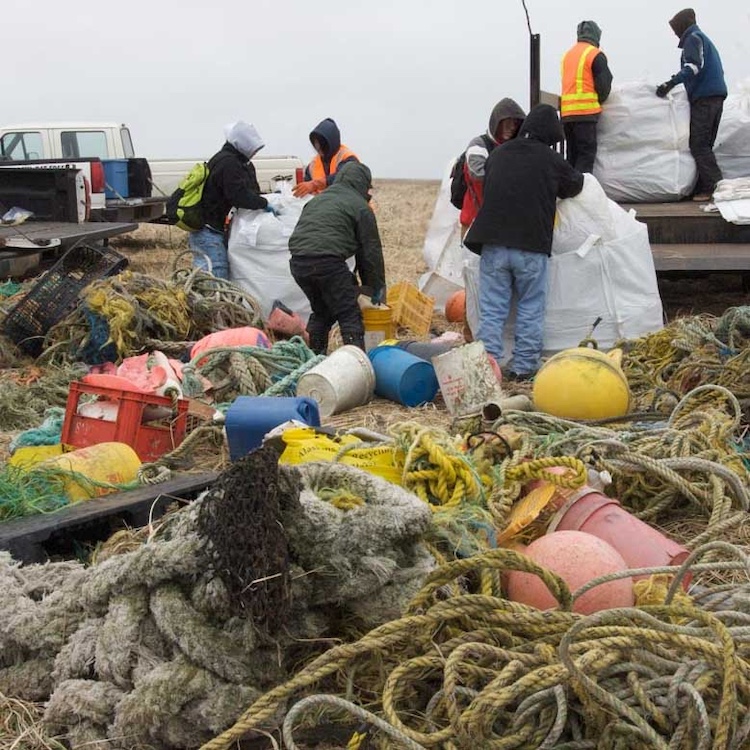 Group on the coast of Alaska gathering up ropes, buckets, garbage, buoys and other marine debris in large bags and loading into trucks.