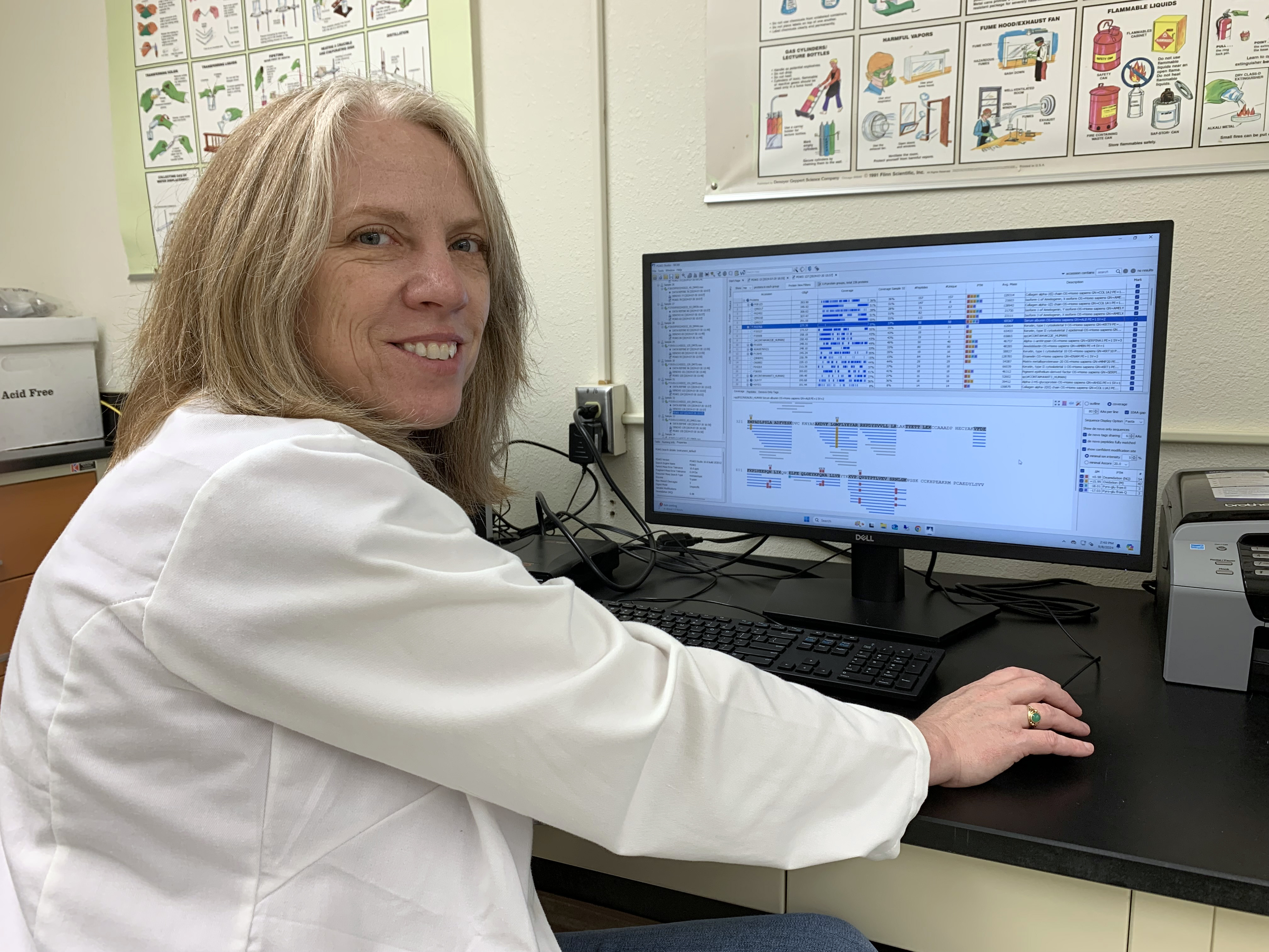 a woman sits at a computer with data and graphs on the screen