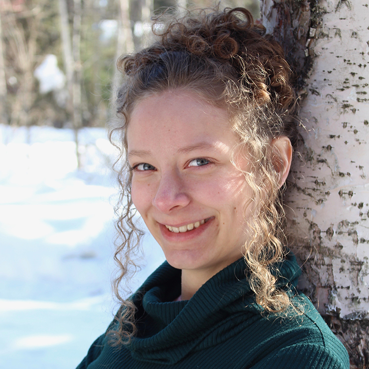 Photo of Tehya McLeod leaning against a birch tree in the Alaskan outdoors during winter.