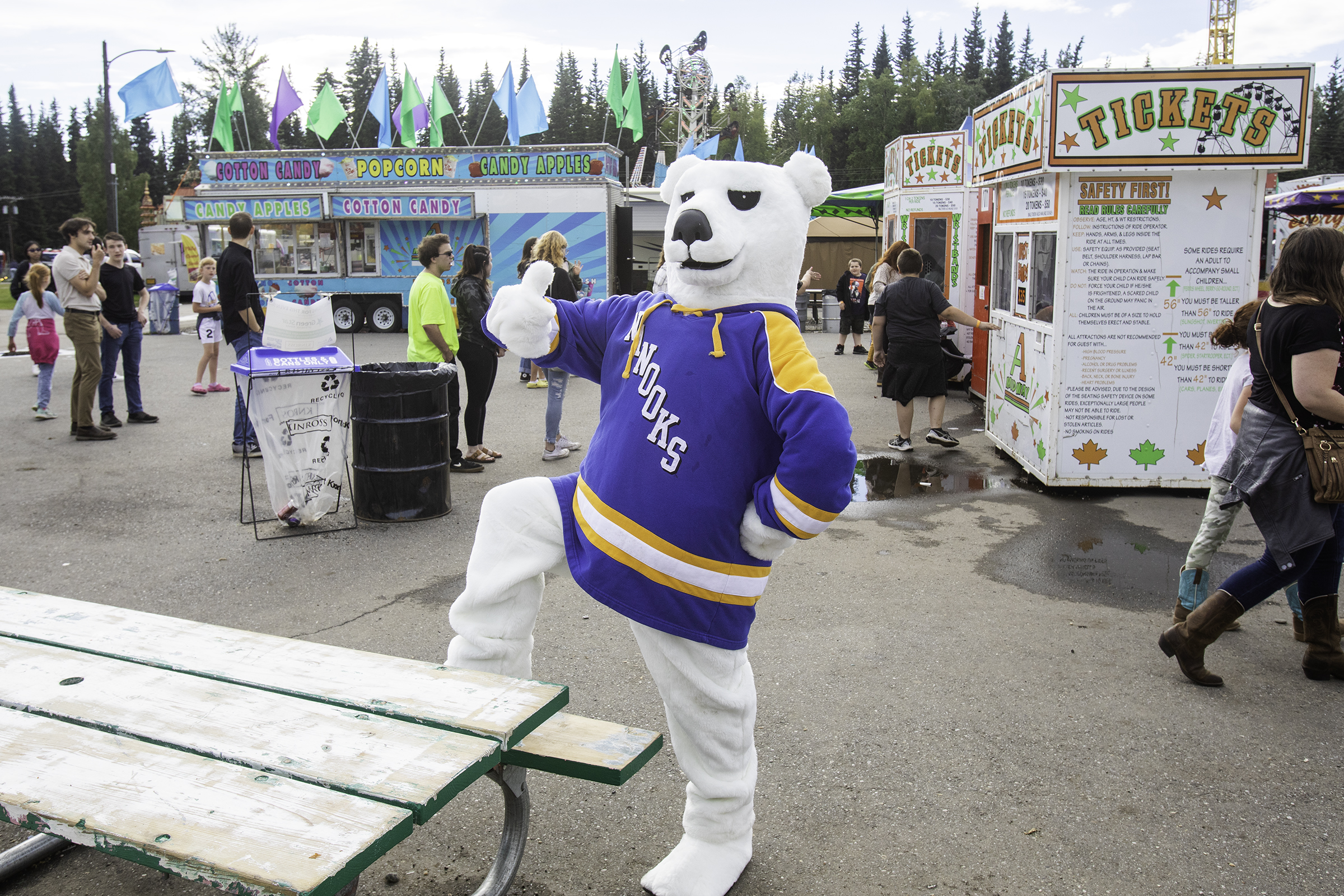 A polar bear mascot wearing a UAF jersey gives a thumbs up while standing on the midway at the fair.