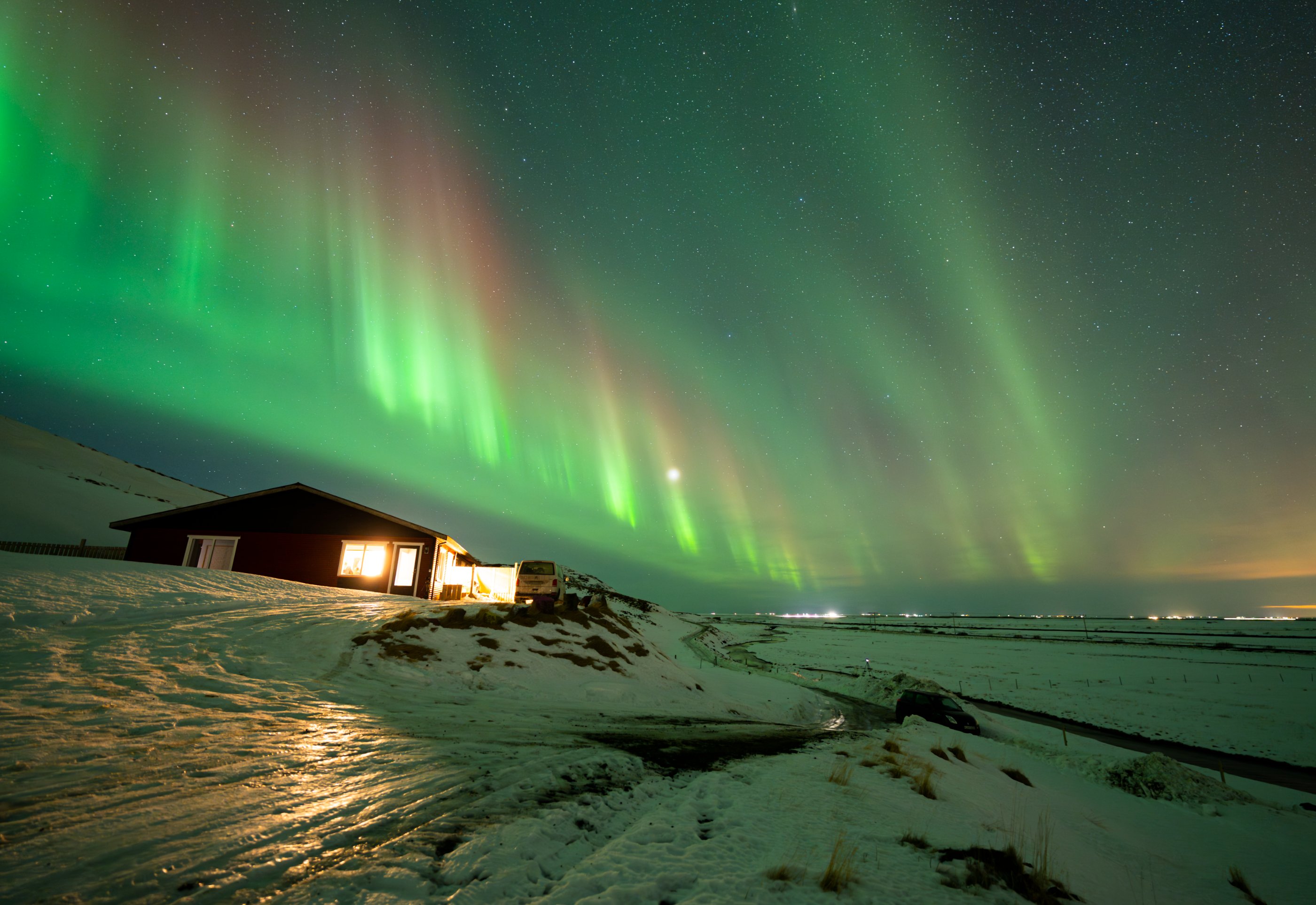 the aurora is in the sky over a cabin and a frozen coastal area