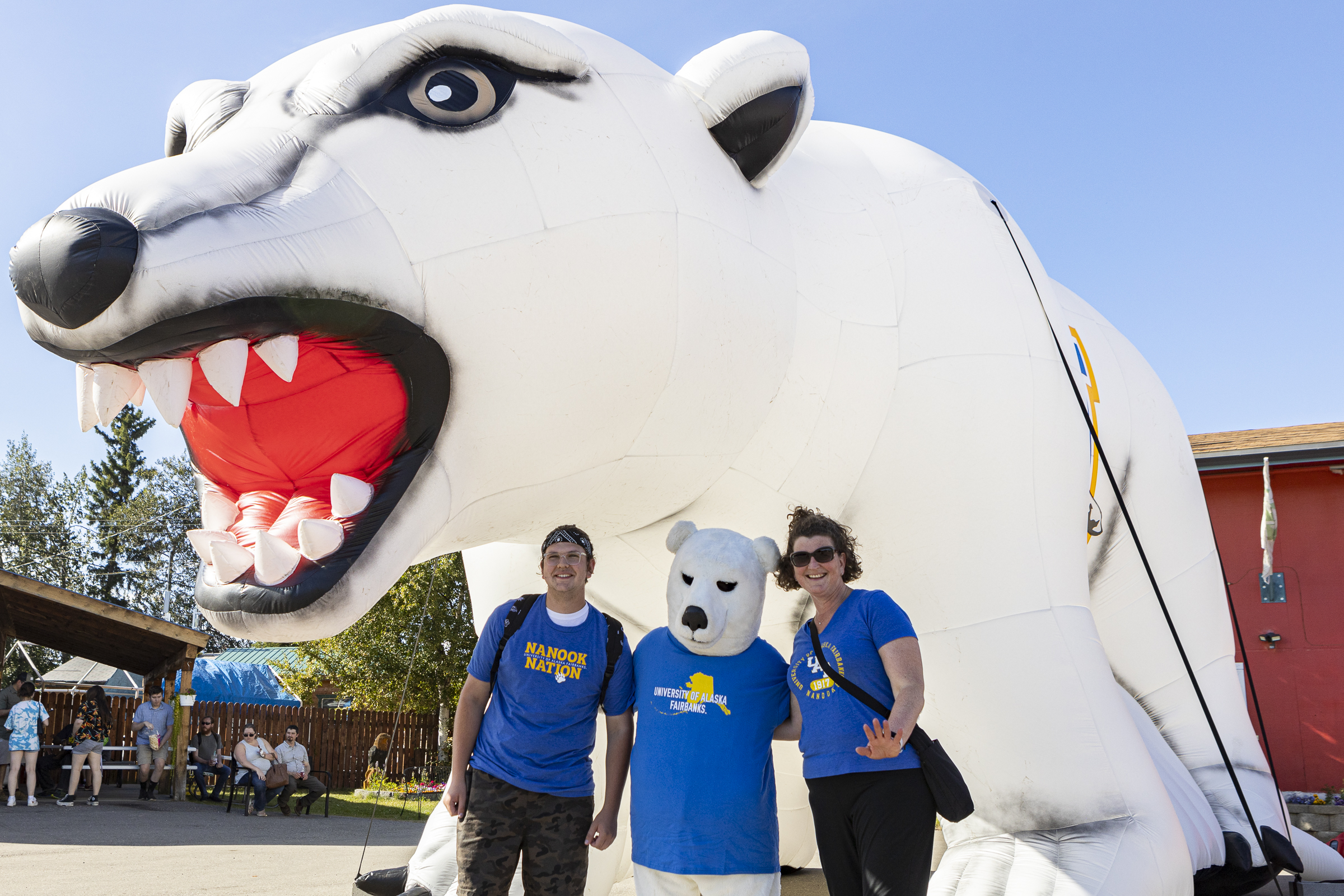 two people stand on either side of a polar bear mascot with a large inflatable polar bear behind them