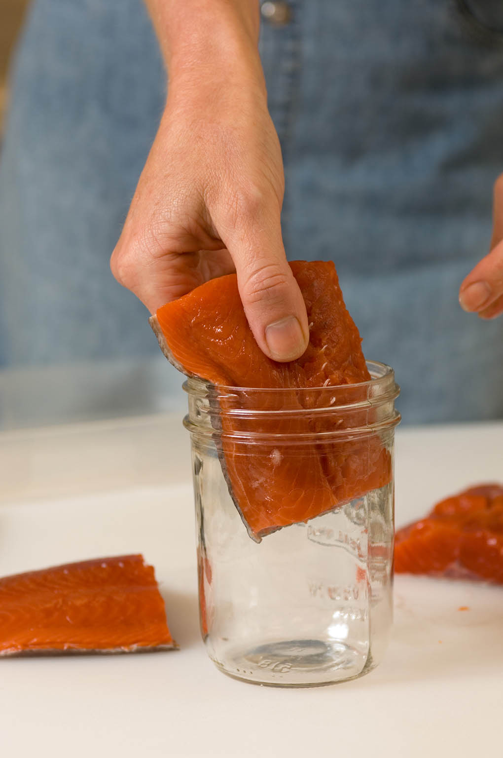 A person inserts a salmon fillet into a canning jar.