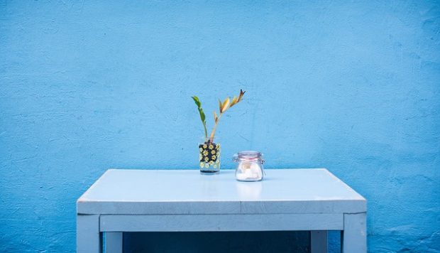 Minimal photo of a rustic blue table with a small vase and sugar jar pushed against a blue wall