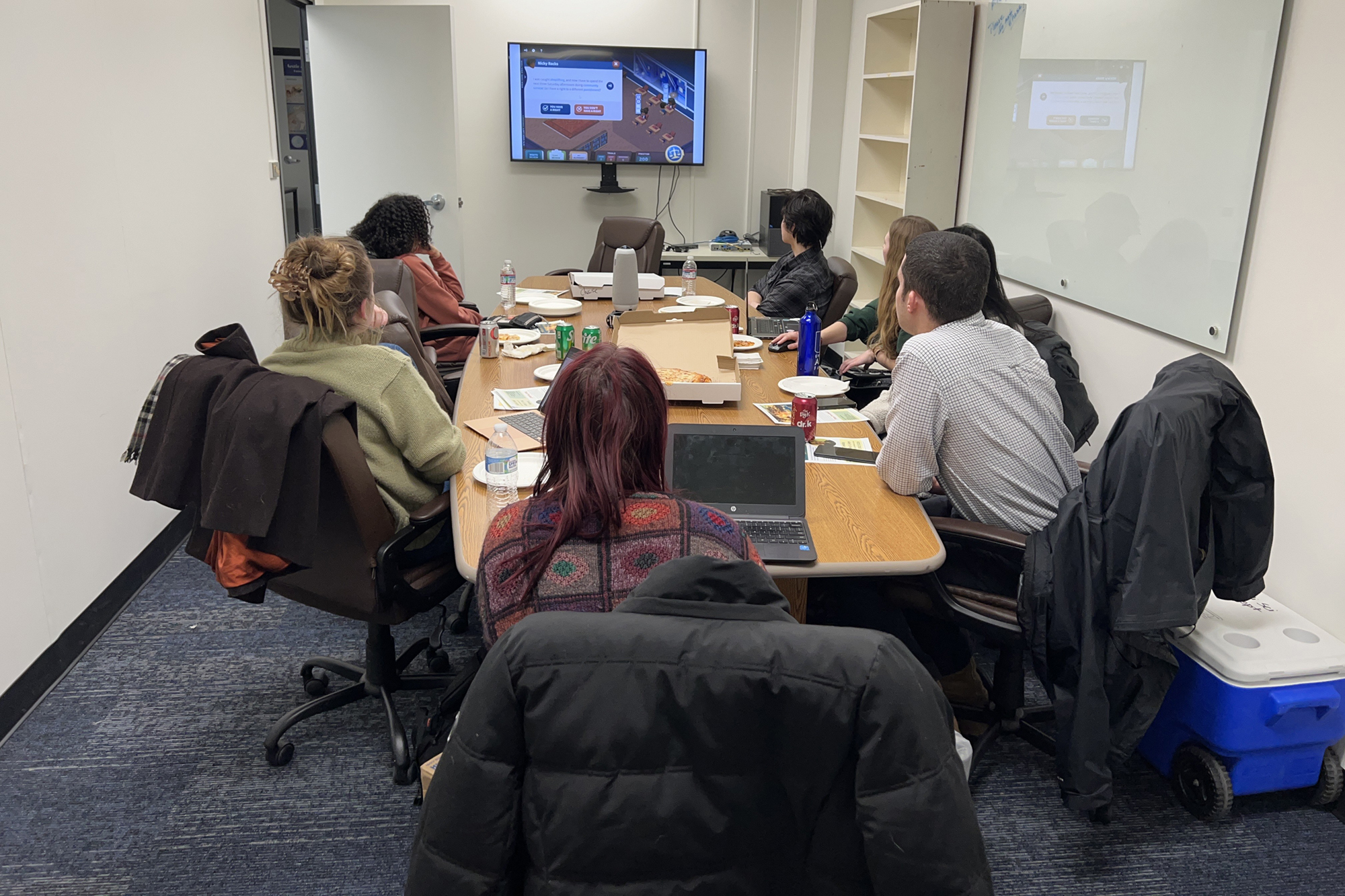 Pre-Law club attendees seated around a table eating pizza while playing an online game which presented different hypothetical scenarios one might encounter at a law office. UAF Photo courtesy of Carol Gray.