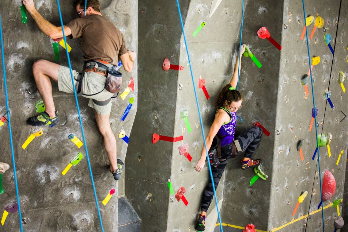 Two climbers climbing at the UAF SRC indoor climbing wall.