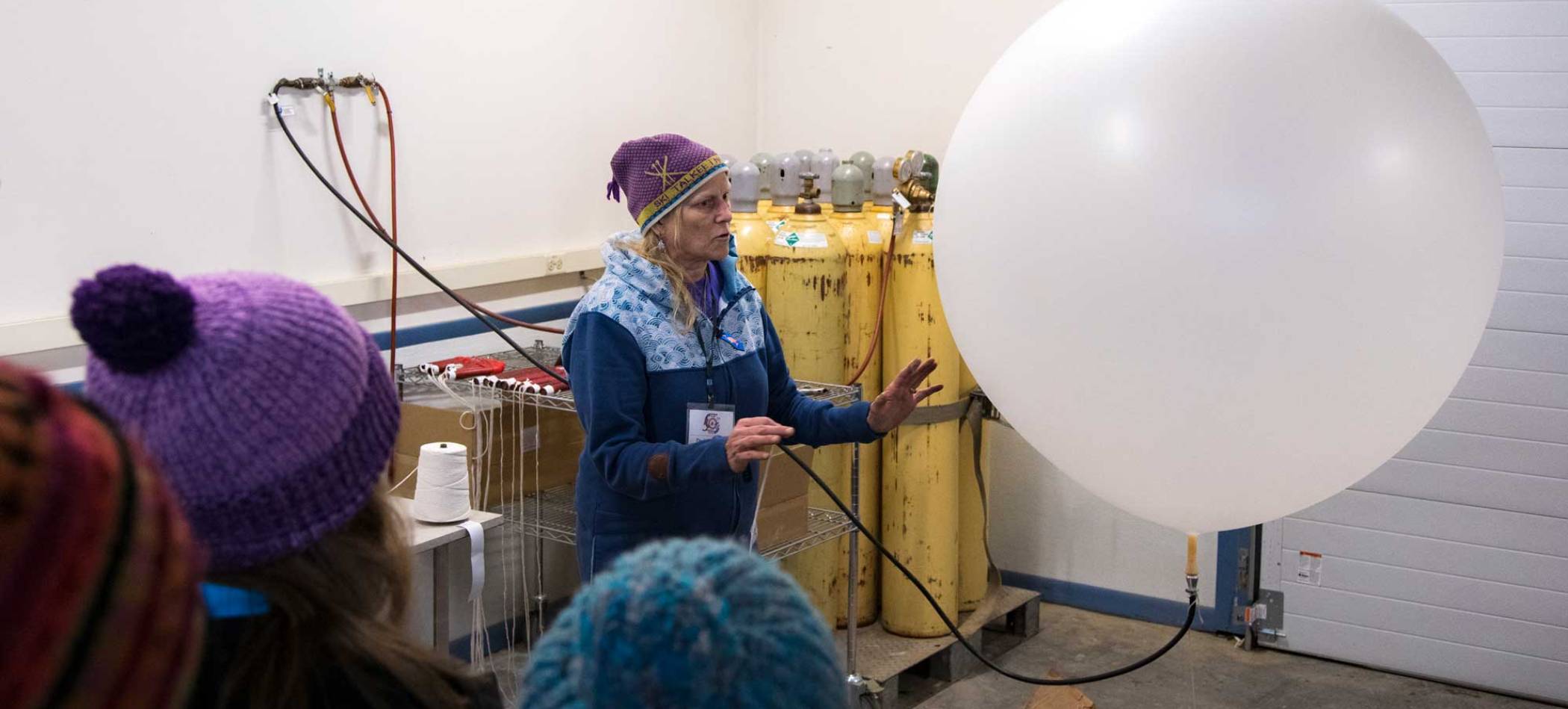 A researcher with a large balloon connected to a hose addresses a crowd