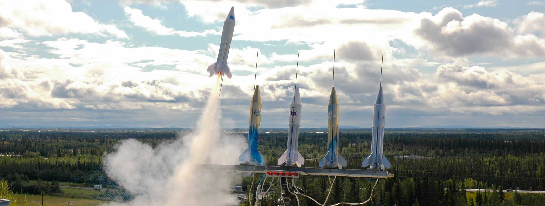 Five small rockets in a row are shown with the first rocket mid-launch