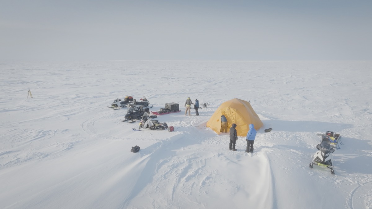 Researchers at a snowy field site with snowmobiles, equipment and a tent.