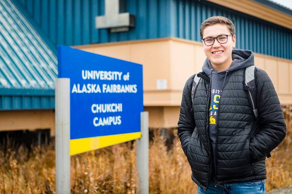 A smiling student standing outside the Chukchi Campus exterior sign