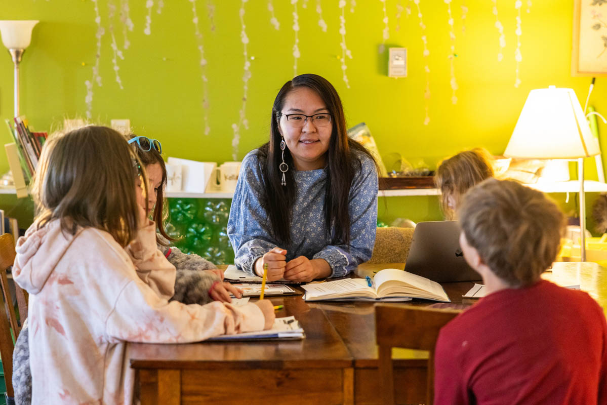 A teacher addresses elementary students gathered at a table