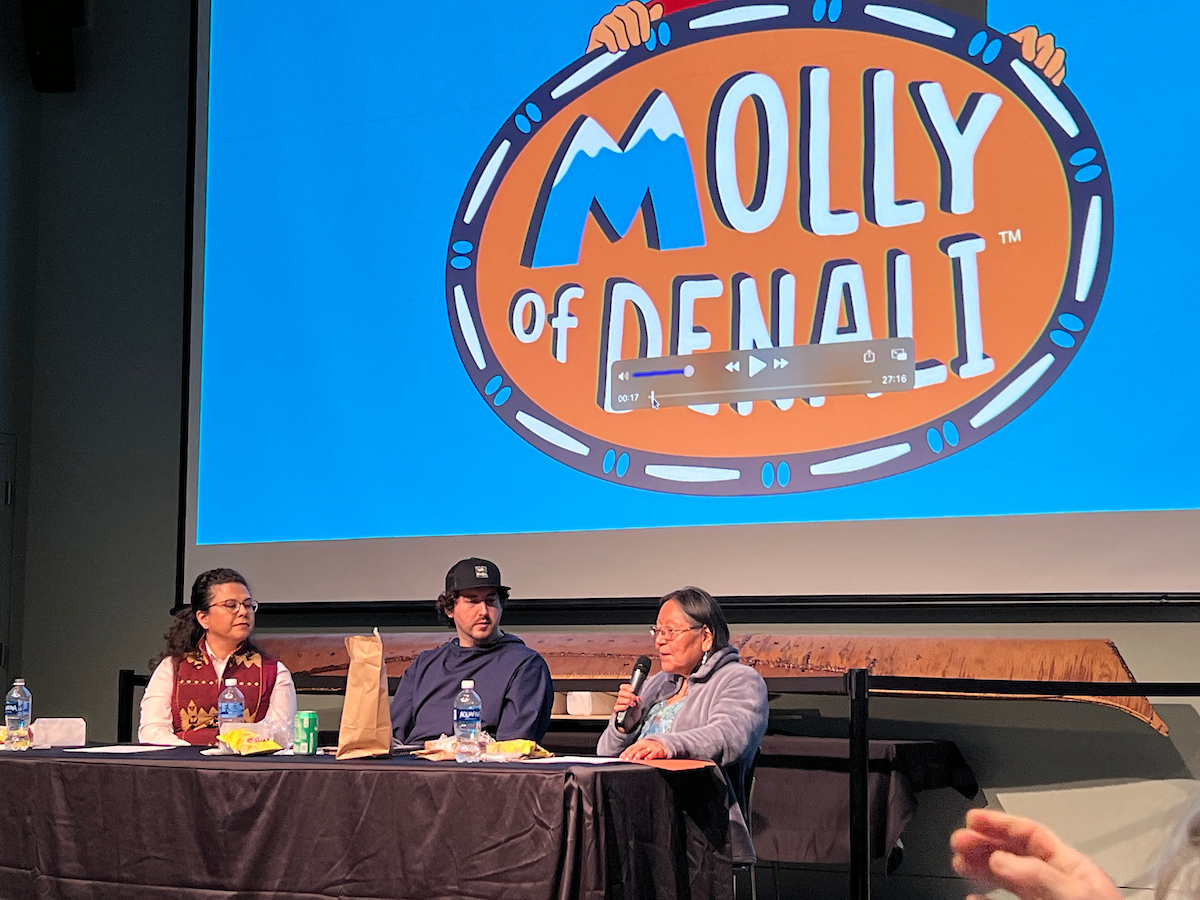 Three people at a panel in front of a screen playing clips from Molly of Denali. UAF photo