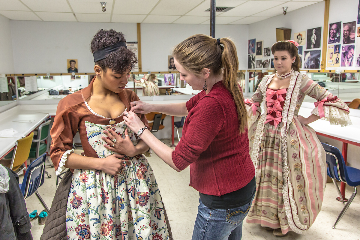 Assistant professor Bethany Marx helps Nicole Cowans into her costume before Cowans, Katrina Kuharich (right) and other members of the cast of Theatre UAF's production of "Tartuffe" performed a live teaser in Wood Center a couple of days before opening night. | UAF Photo by Todd Paris, 2014