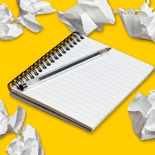 Blank notebook and pen surrounded by crumpled paper on a yellow background