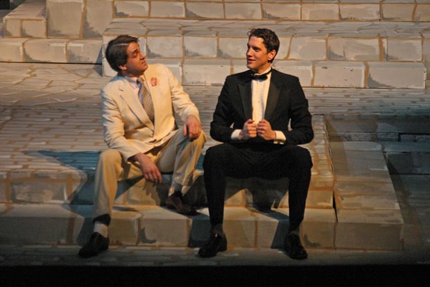 On stage, two men sit on the steps engaged in a conversation.