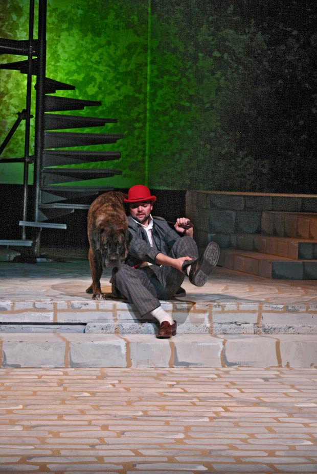 An unexpected moment of companionship captured on stage: a man adjusts his shoe as his loyal dog stands next to him.