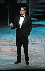 Raising a toast;  a man on stage holds a champagne glass, his gaze looking beyond the audience.