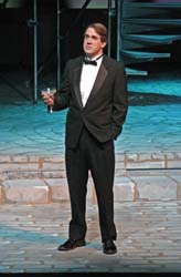 Raising a toast;  a man on stage holds a champagne glass, his gaze looking beyond the audience.
