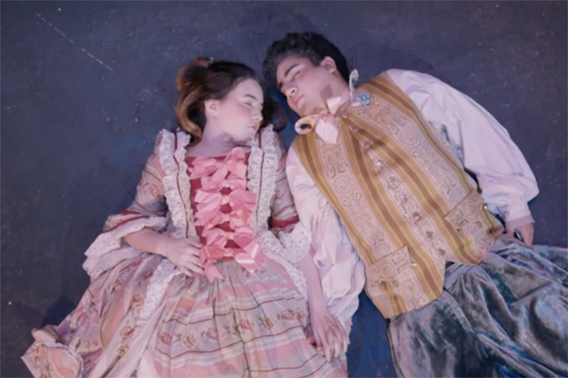 Pink Violet characters Dana (played by Isabelle Nygren) and Billy (played by Charles Wolgemuth) lay on stage in costume. UAF still from the Pink Violet trailer. 