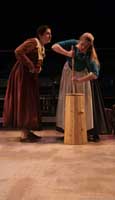 Actors on stage during the 2010 production of Vinegar Tom. One actress leans in to talk to another actress who is churning butter.| Photo courtesy of Stephan Golux