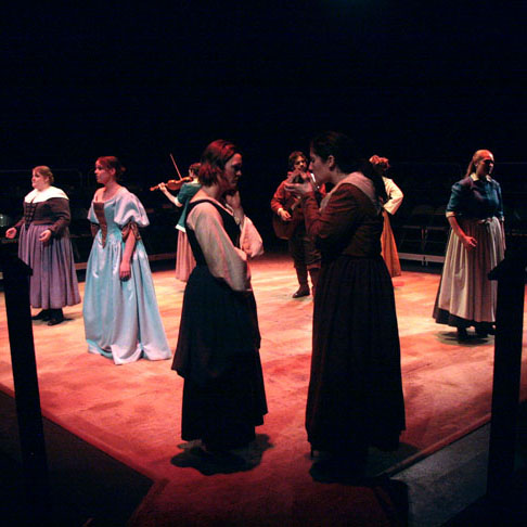 Actors on stage during UAF Theatre and Film's production of Vinegar Tom. Two actresses stand off, face to face in the center. Other actresses in costume flank the sides of the stage. Photo courtesy of Stephan Golux