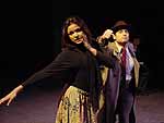 Two actors on stage during the Winter Shorts production of Cop-Out, one is a woman dancing and the other is dressed in a suit standing slightly behind her | UAF Photo by Kade Mendelowitz