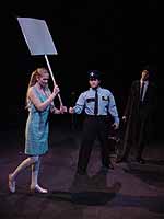 Two actors on stage during the Winter Shorts production of Cop-Out, an officer points at a woman walking across the stage holding a sign | UAF Photo by Kade Mendelowitz