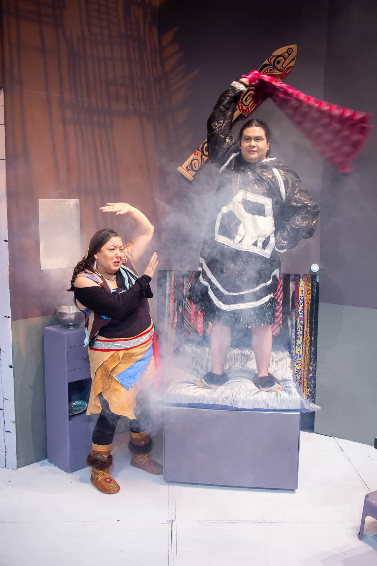 Two actors stand on stage with a smoke effect surrounding them