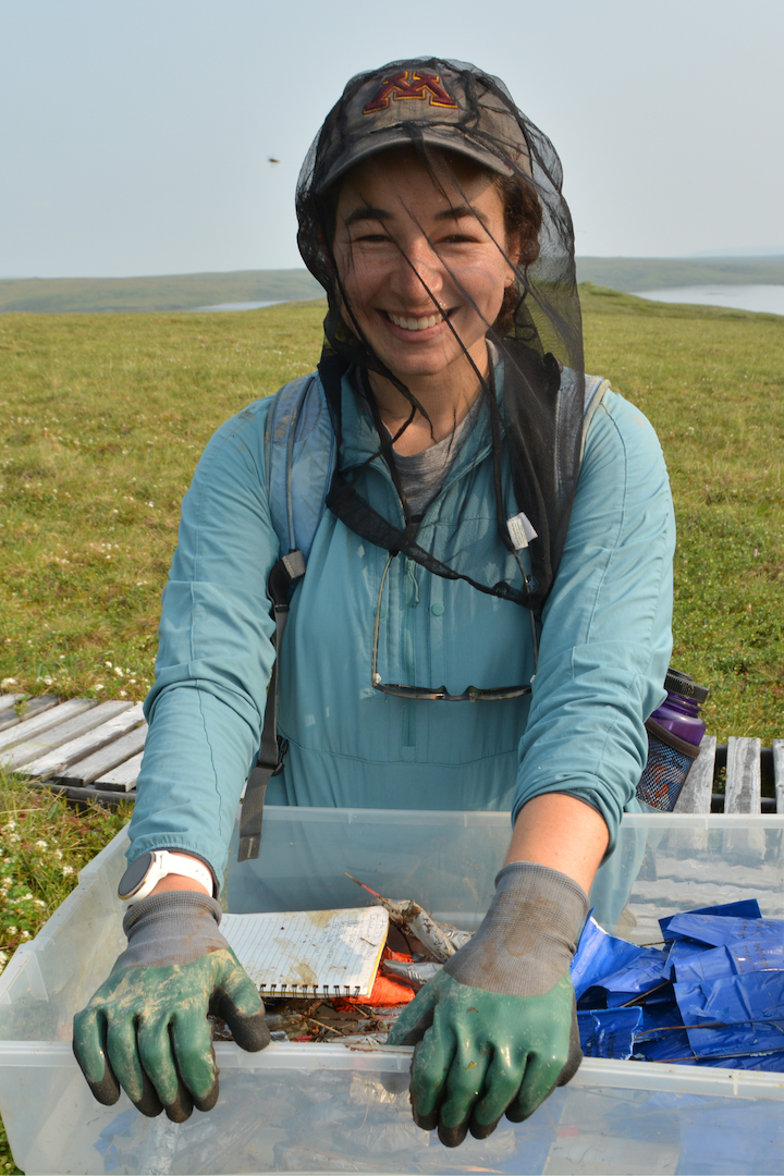 woman in bug head net holding science supplies in tundra