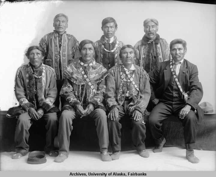 Group portrait of Athabascan Chiefs adorned with traditional garments, and ornaments.