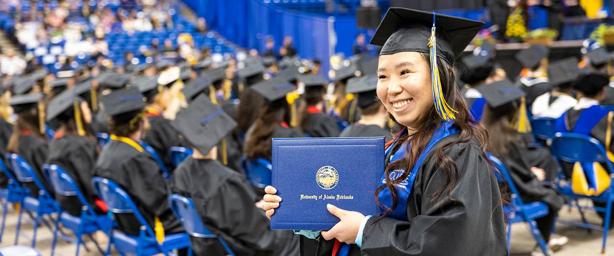 A graduating student displays their diploma cover for a photo at the 2022 UAF Commencement Ceremony at the Carlson Center in Fairbanks.
