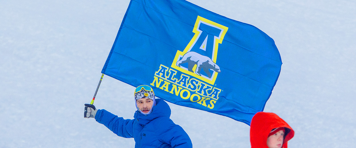 A supporter waves an Alaska Nanooks flag at the 2024 Nordic Cup cross country ski races