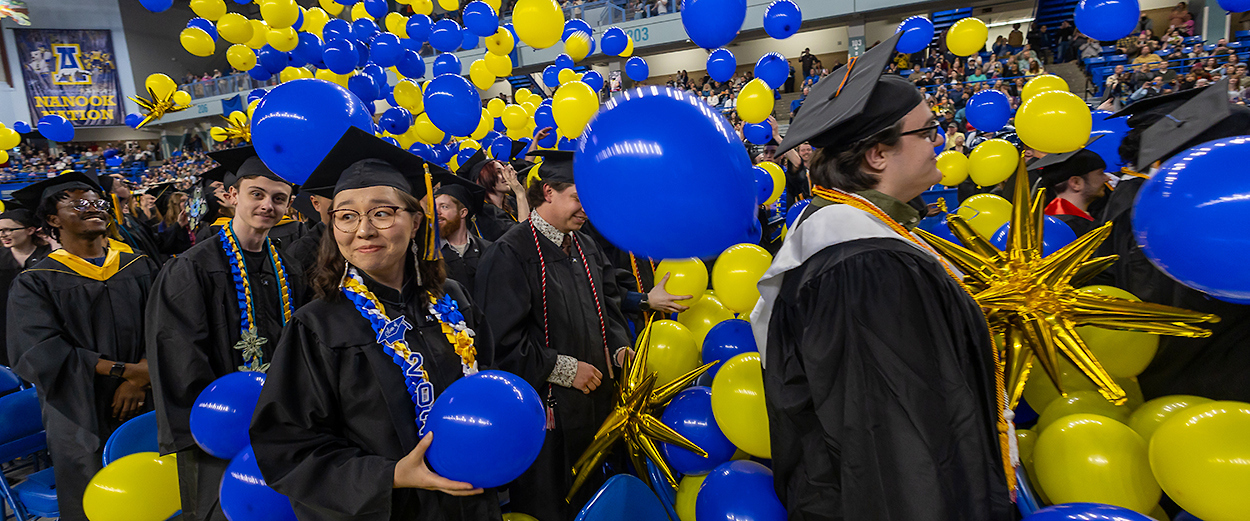 Graduating UAF students smile as blue and gold balloons drop from the Carlson Center ceiling at the end of the 2026 Commencement Ceremony