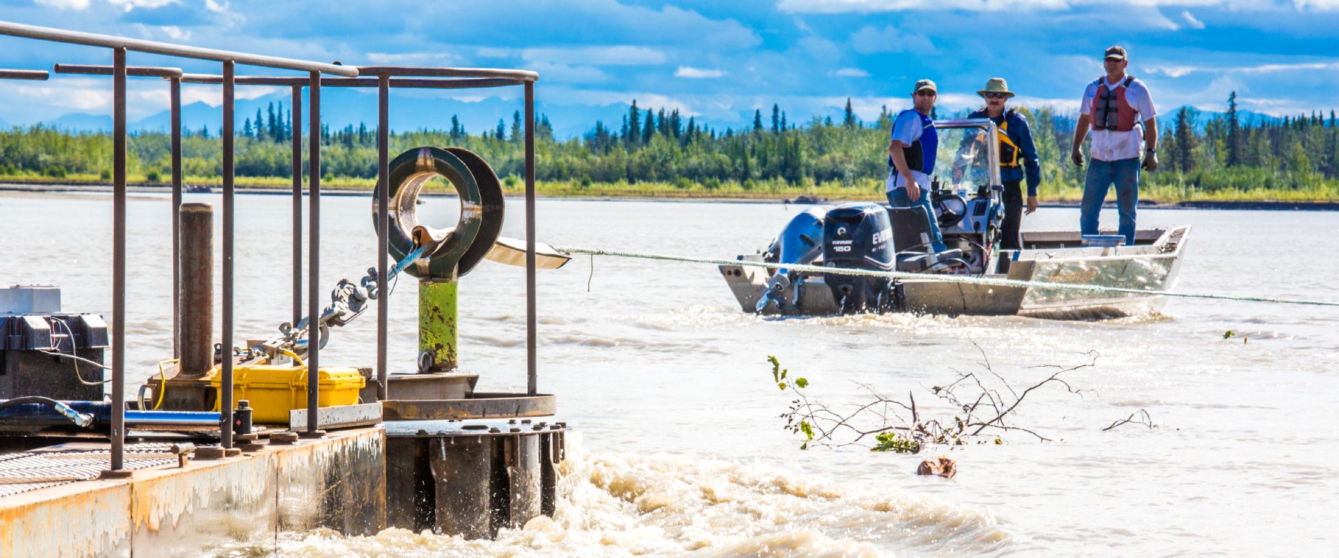 Researchers with UAF's School of Fisheries and Ocean Sciences and the Alaska Center for Energy and Power (ACEP) watch as debris hits a prototype deployment boom on a barge anchored in the Tanana River near Nenana.