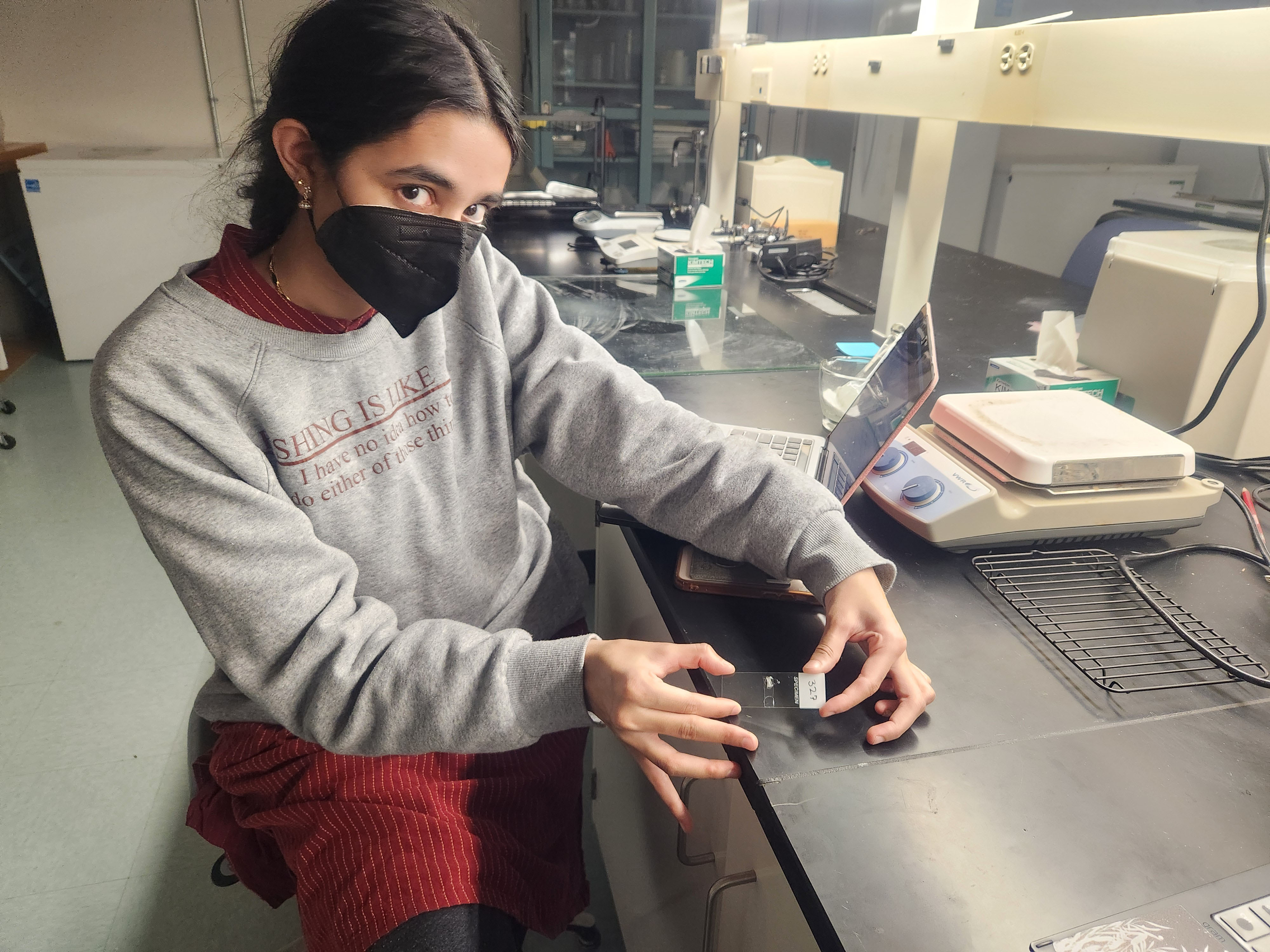 Nivedita Menon holds a microscope slide that she has mounted an otolith onto for Sr isotope analysis.