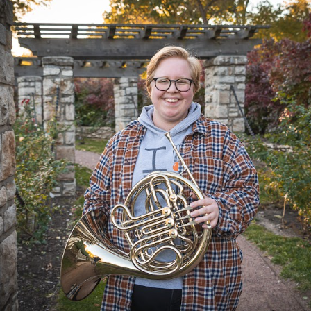 Beatrice standing outside and holding a french horn.
