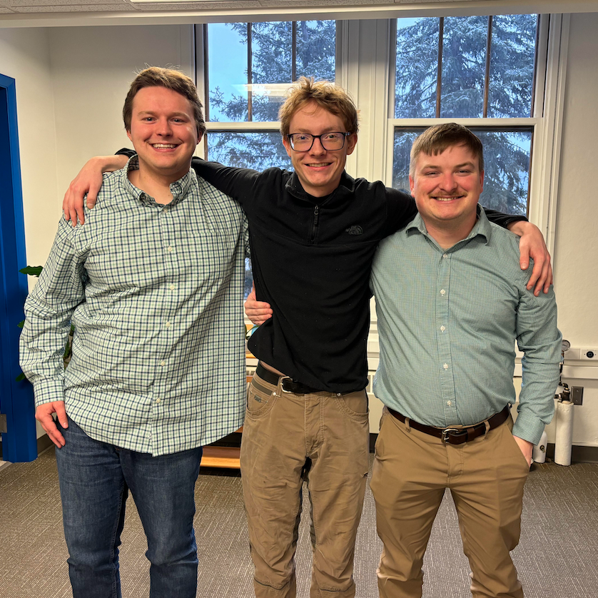 Three gentlemen pose for a photo in front of windows