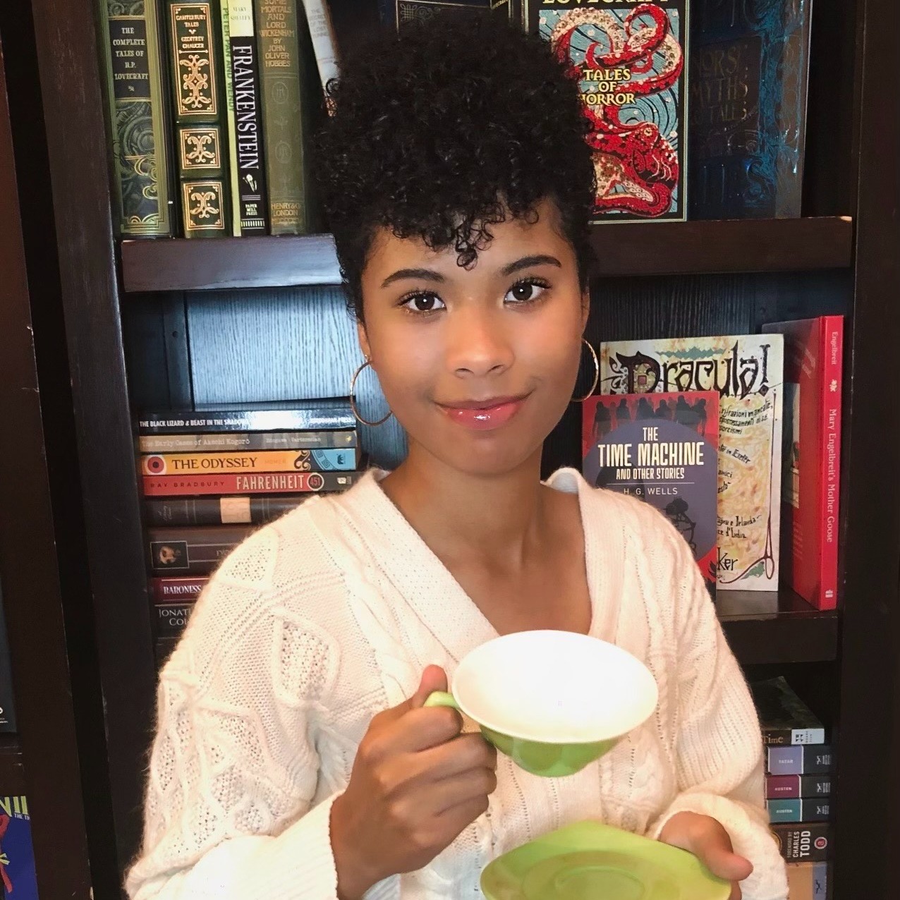 Naomi in front of a bookshelf with a tea cup