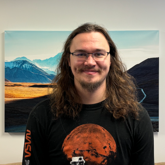 Image of Tane standing in front of a landscape photo of Alaska